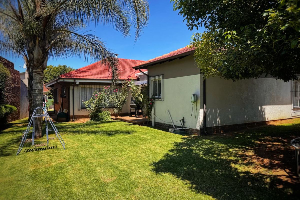 A view of the rear garden and house exterior, featuring a tiled roof, security bars on windows, and a well-maintained lawn area.