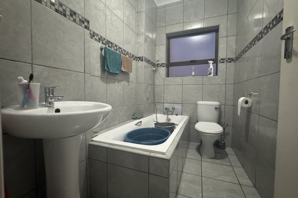 A functional bathroom featuring a pedestal basin, built-in bathtub, and toilet, finished with neutral grey wall and floor tiling.