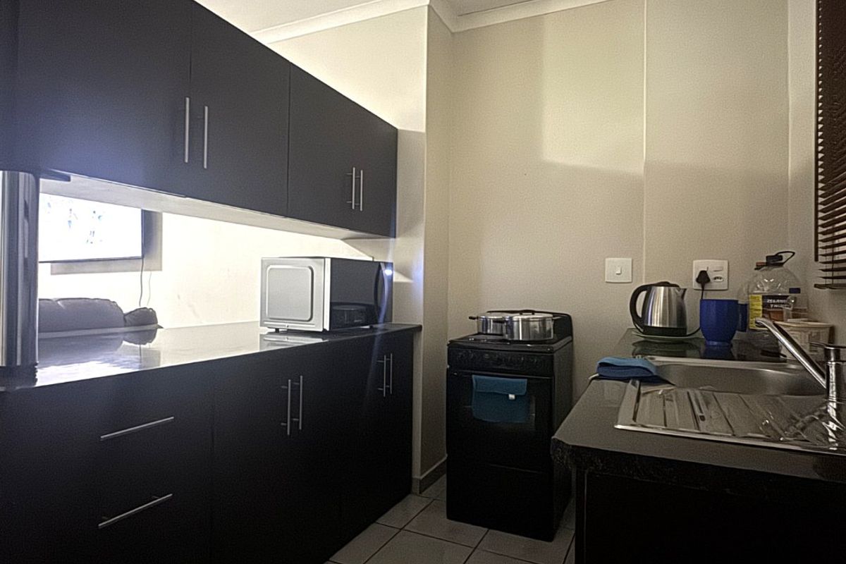Compact kitchen featuring dark cabinetry, granite countertops, tiled flooring, and a freestanding stove, offering a functional workspace.