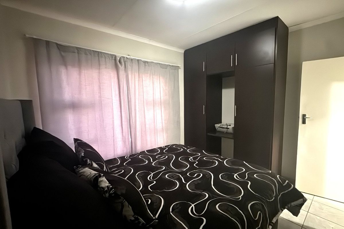 A bedroom featuring built-in dark wood cupboards, tiled flooring, and neutral wall finishes.