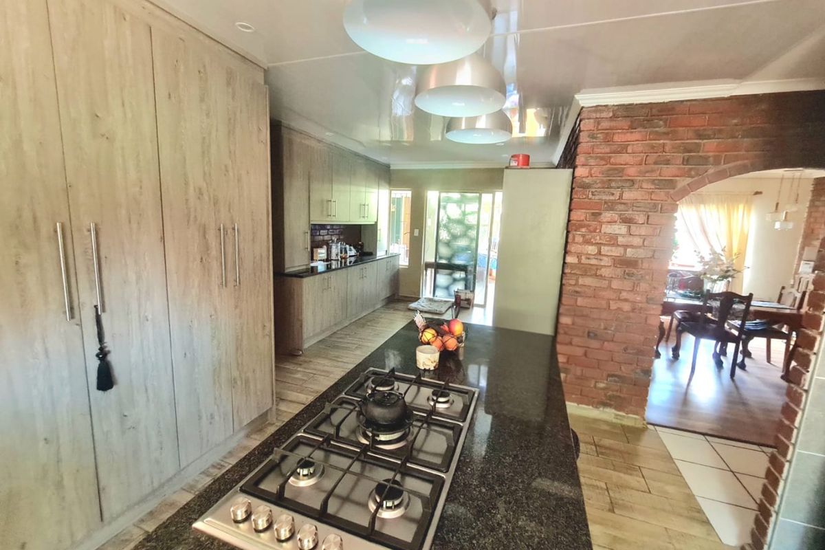 Modern kitchen featuring wood-finish cabinetry, granite countertops with an integrated gas hob, and a distinctive exposed brick archway leading to the dining area.