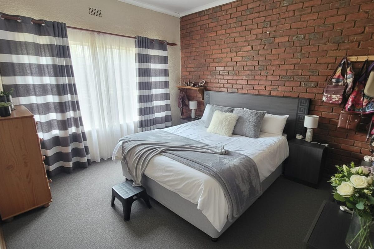 A bedroom featuring an exposed brick feature wall, carpeted flooring, and natural light through a large window.