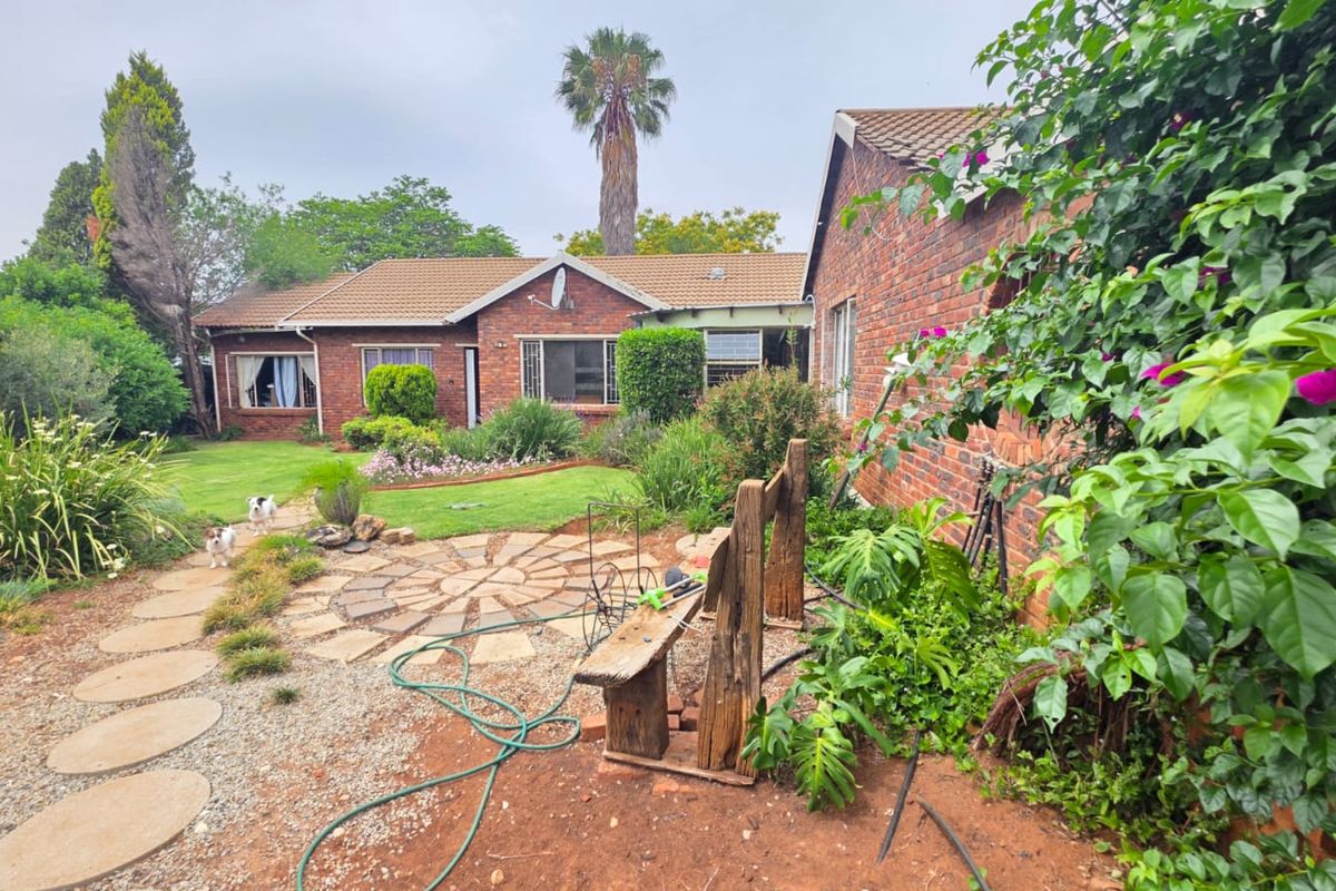 A rear view of a brick house featuring a landscaped garden, stone paved patio area, and established greenery.