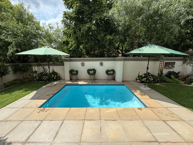 A well-maintained swimming pool area featuring a tiled surround, landscaped garden, and a decorative boundary wall.