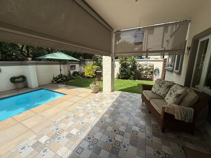 Covered patio area featuring patterned floor tiles, retractable blinds, and direct access to a private swimming pool and landscaped garden.