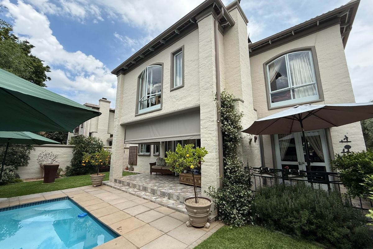 Rear view of a two-story residence featuring a paved patio area, swimming pool, and well-maintained stucco exterior with arched windows.