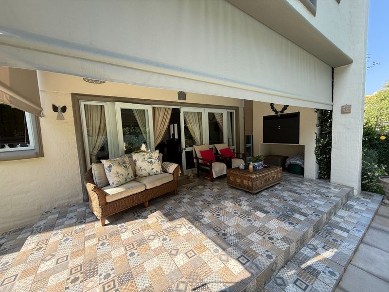 Covered patio area featuring patterned floor tiles, a built-in braai, and a retractable awning, providing a seamless transition to the interior living space.