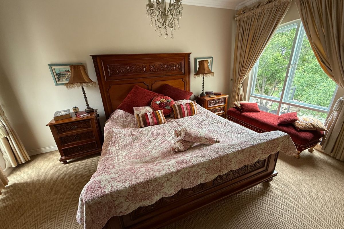 A well-maintained bedroom featuring carpeted flooring, a large window providing natural light, and decorative coving with a central chandelier.