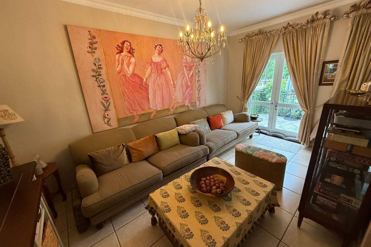 A cozy living room featuring tiled flooring, a classic crystal chandelier, and direct access to the outdoor area through glass french doors.