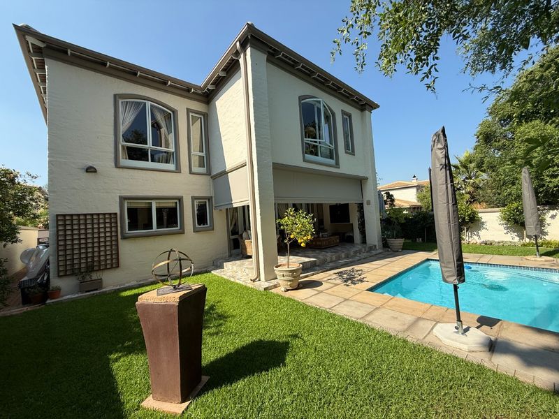 Rear view of a two-story house featuring a swimming pool, stone-paved patio area, and well-maintained lawn.