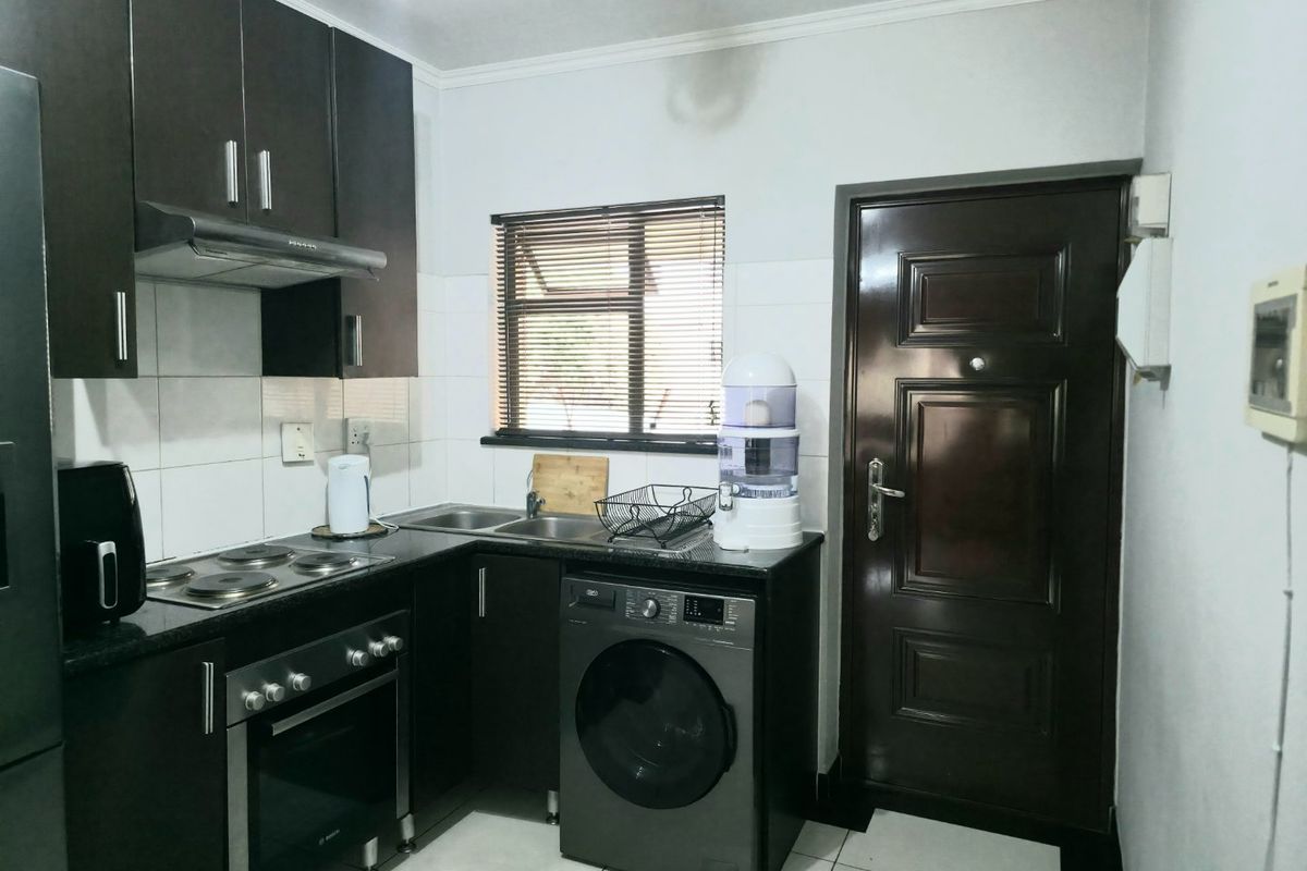 Compact kitchen featuring dark wood cabinetry, granite countertops, built-in oven, electric hob, and integrated laundry space with tiled finishes.