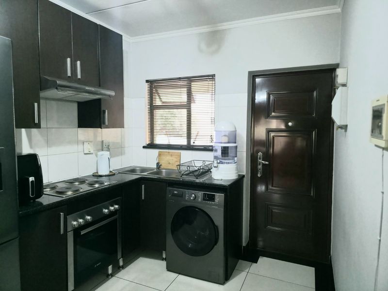 Compact kitchen featuring dark wood cabinetry, granite countertops, built-in oven, electric hob, and integrated laundry space with tiled finishes.