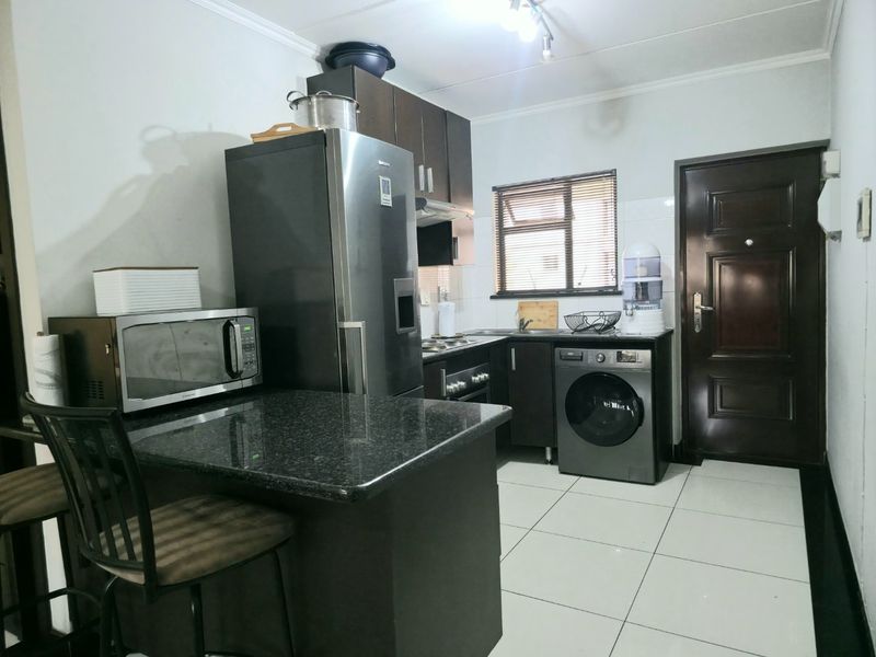 Compact kitchen featuring dark cabinetry, granite countertops, tiled flooring, and integrated appliances, providing a functional workspace with direct access to the exterior.