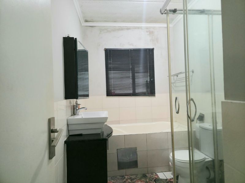 A functional bathroom featuring a vanity with vessel sink, bathtub, separate shower enclosure, and toilet, showing signs of water damage on the ceiling and walls.