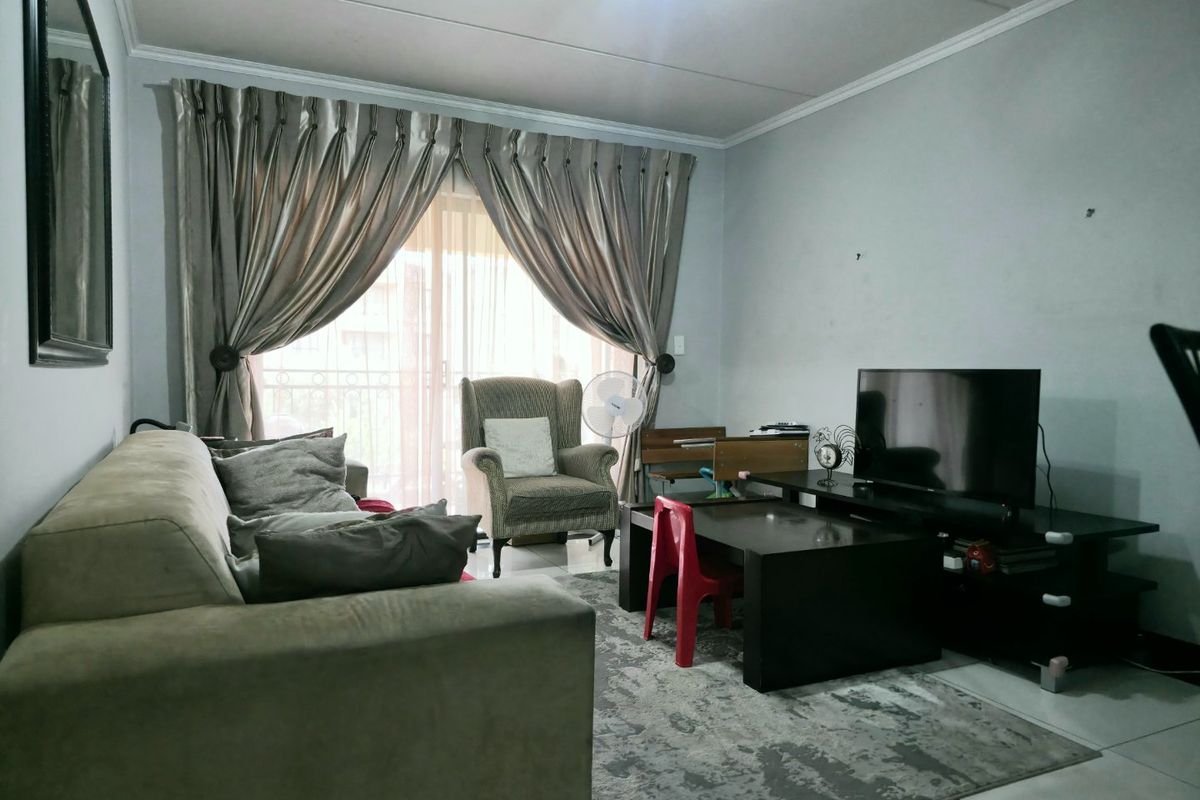 A living room featuring tiled flooring, coved ceilings, and a sliding glass door providing access to a balcony.