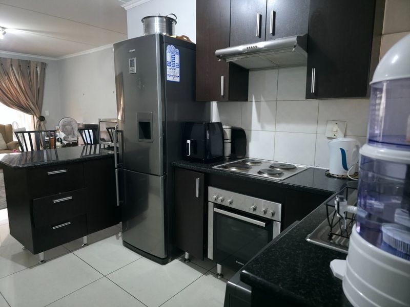 A functional kitchen featuring dark wood cabinetry, granite countertops, built-in oven, electric hob, and stainless steel extractor fan with tiled flooring.