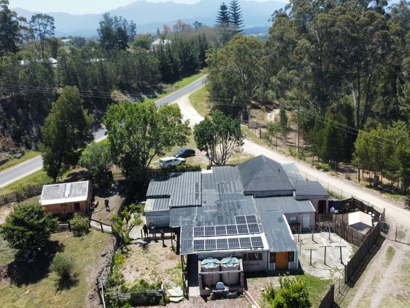 Aerial view of a farm property featuring a main dwelling with solar panels, water storage tanks, and surrounding rural landscape.