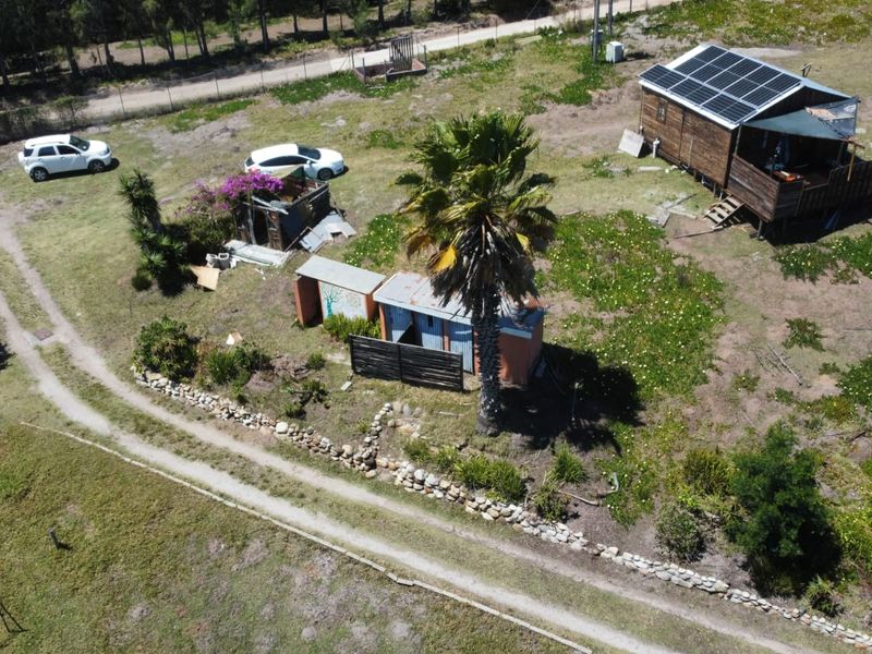 Aerial view of a farm property featuring a cabin with solar panels, timber decking, and various outbuildings set within a rural landscape.