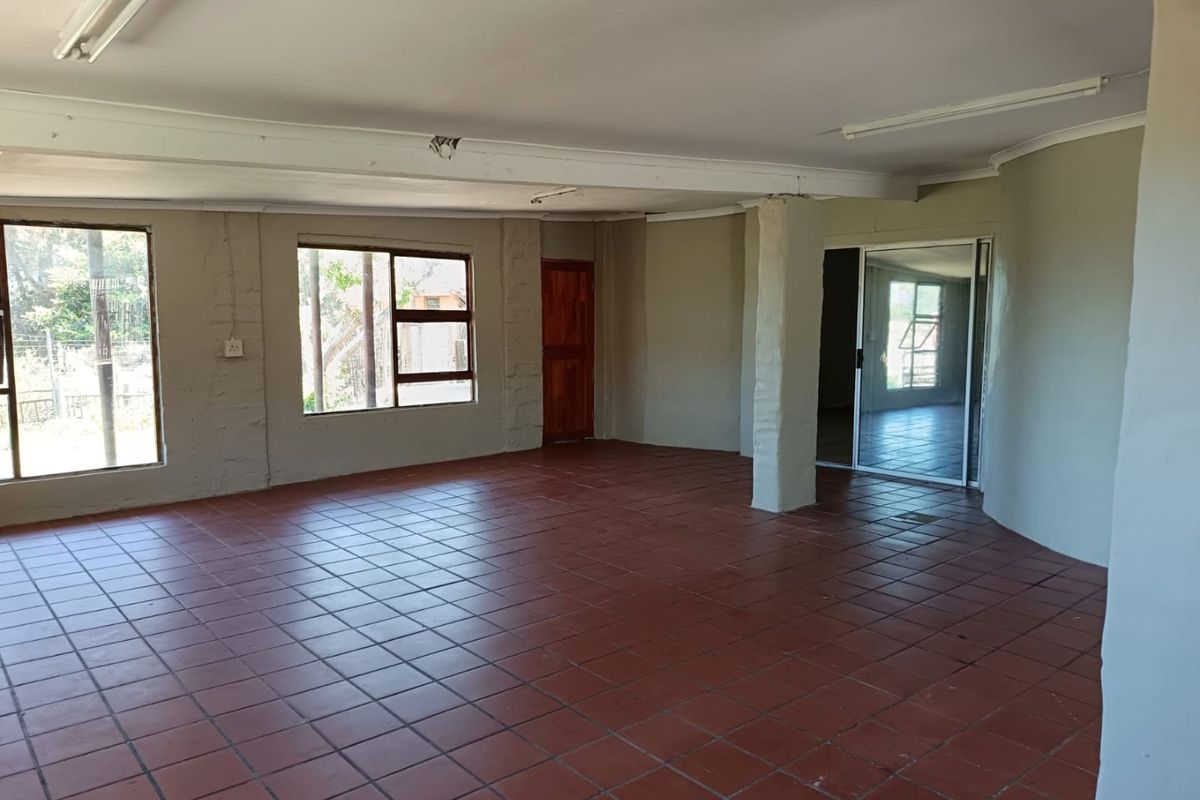 A spacious, empty living area featuring terracotta floor tiles, structural columns, and large windows providing natural light, ready for renovation or staging.