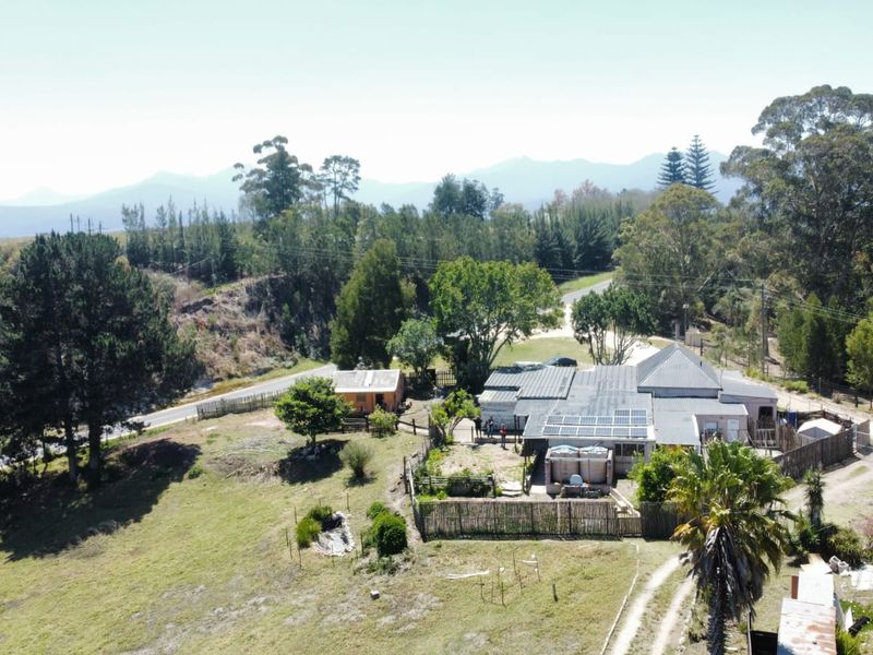 Aerial view of a farm property featuring a main dwelling with solar panels, water tanks, and surrounding rural landscape.