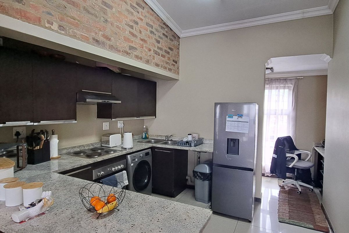 A functional kitchen featuring granite countertops, dark cabinetry, an exposed brick accent wall, and integrated appliances, with an open-plan layout.