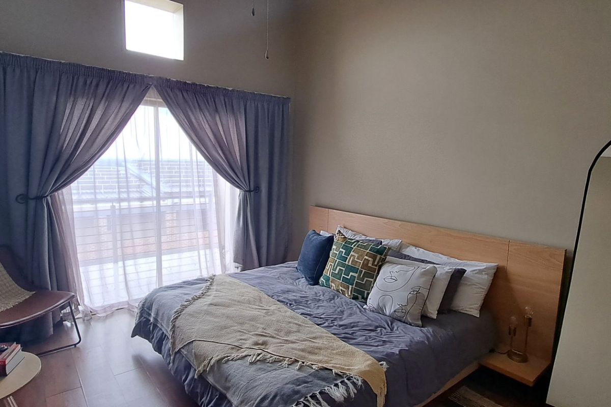 A well-lit bedroom featuring laminate flooring, a built-in headboard, and a sliding glass door providing access to an outdoor area.
