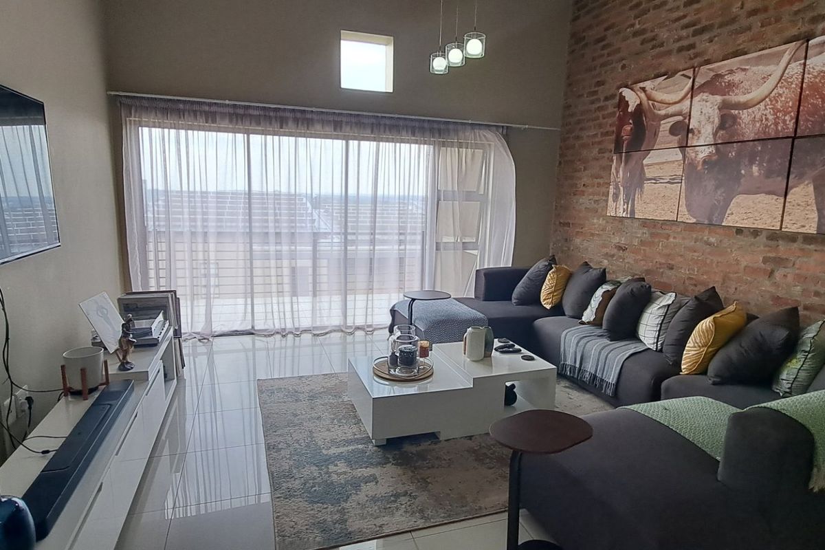 A modern living room featuring an exposed brick wall, large sliding glass doors leading to a balcony, and polished tiled flooring.