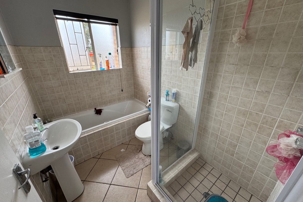 A functional bathroom featuring a pedestal basin, a built-in bathtub, and a separate glass-enclosed shower with neutral wall and floor tiling.