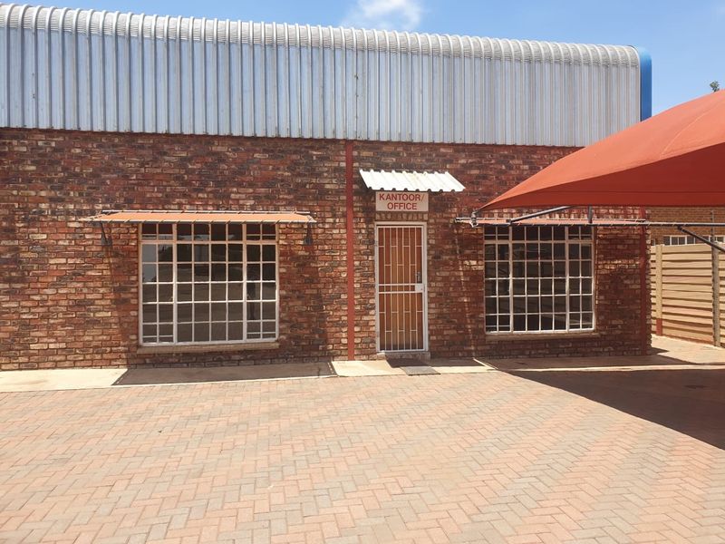 Industrial office entrance featuring a face brick facade, security gates, and a paved driveway with a shade sail.