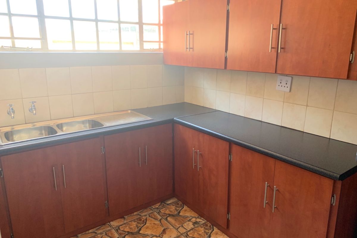 A functional kitchen area featuring wooden cabinetry, a double stainless steel sink, tiled backsplash, and stone-look floor tiles.