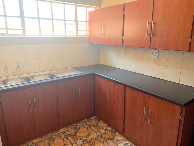 A functional kitchen area featuring wooden cabinetry, a double stainless steel sink, tiled backsplash, and stone-look floor tiles.