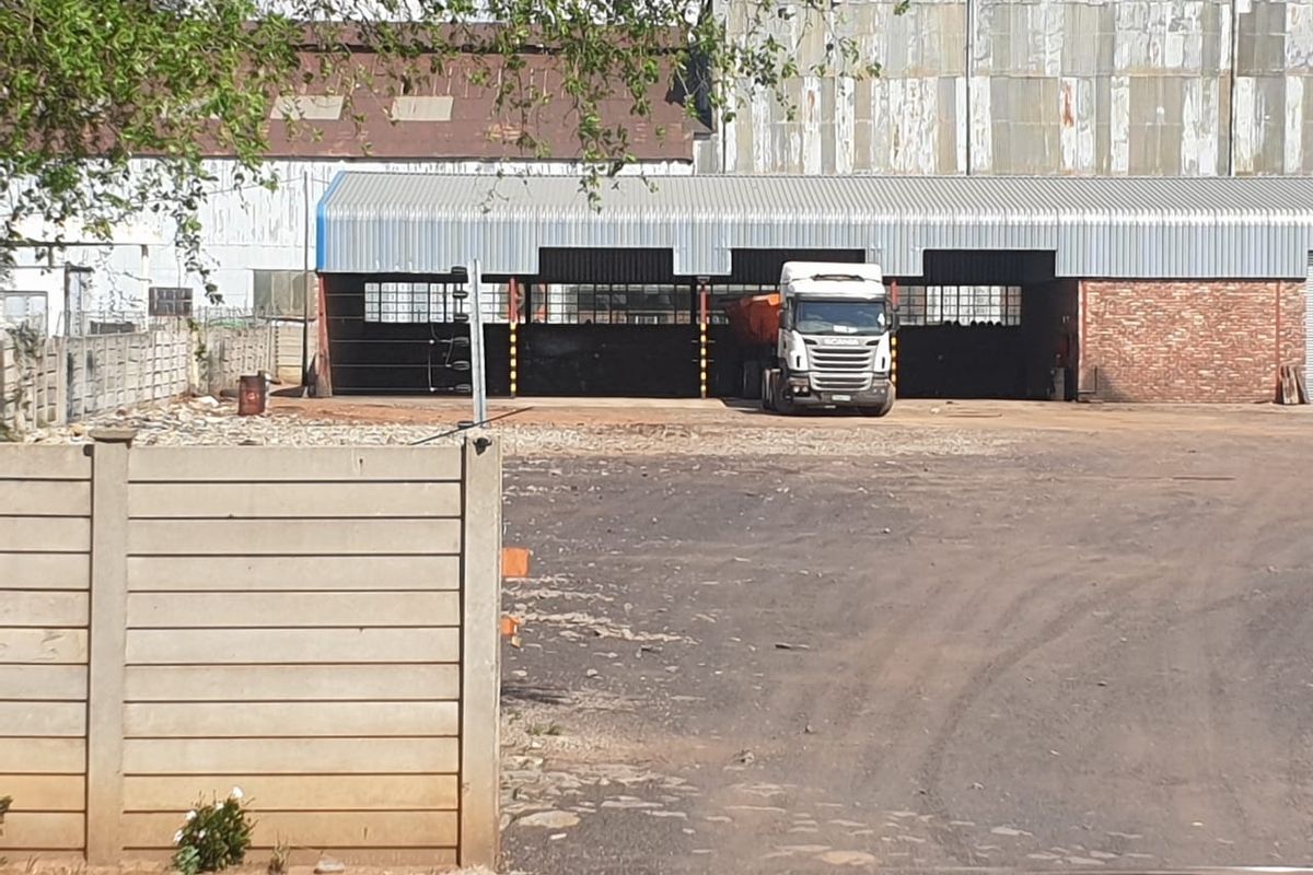 Industrial property featuring an open-sided shed structure with corrugated metal roofing and brick masonry, set within a large unpaved yard area.