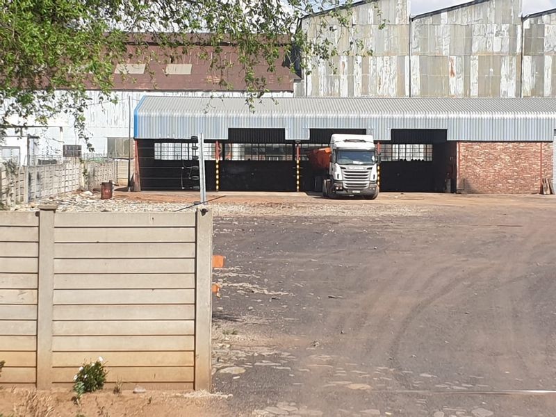 Industrial property featuring an open-sided shed structure with corrugated metal roofing and brick masonry, set within a large unpaved yard area.