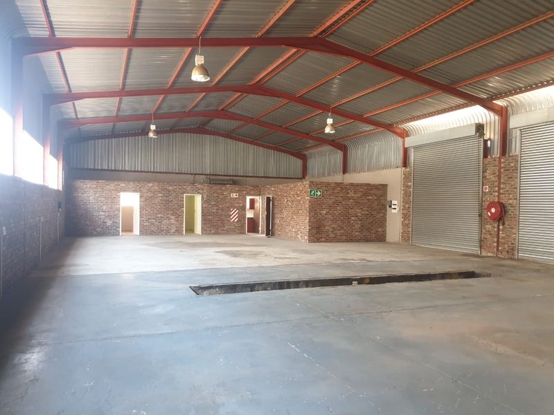 Spacious industrial warehouse featuring exposed brick walls, high-clearance corrugated metal roofing, concrete flooring, roller shutter doors, and a built-in vehicle inspection pit.
