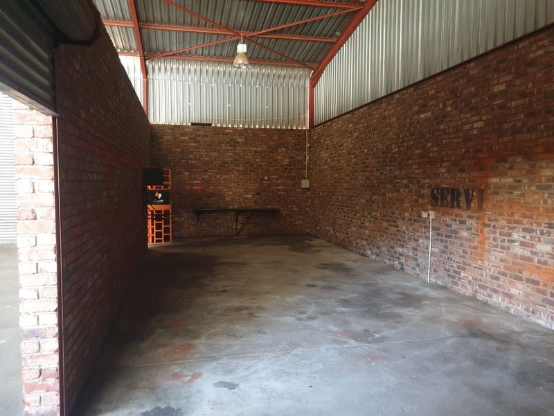 Spacious industrial utility area featuring exposed brick walls, concrete flooring, and high corrugated metal ceilings, suitable for storage or workshop use.