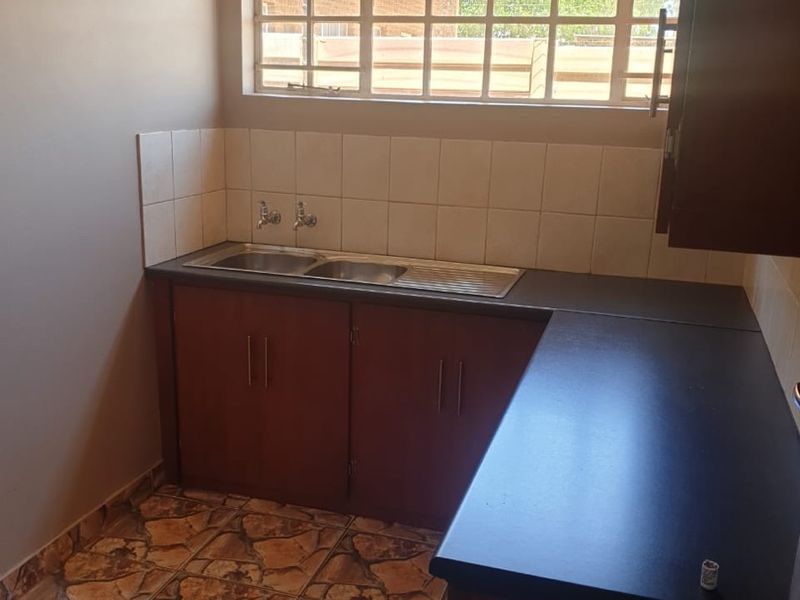 A functional kitchen area featuring built-in cabinetry, a stainless steel double sink, tiled splashback, and durable tiled flooring.