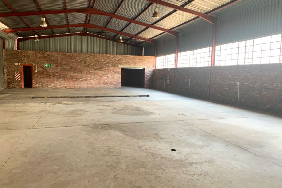 Spacious industrial warehouse unit featuring exposed brick walls, concrete flooring, high steel truss ceilings, and an integrated inspection pit for vehicle maintenance.