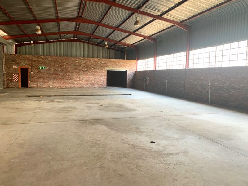 Spacious industrial warehouse unit featuring exposed brick walls, concrete flooring, high steel truss ceilings, and an integrated inspection pit for vehicle maintenance.