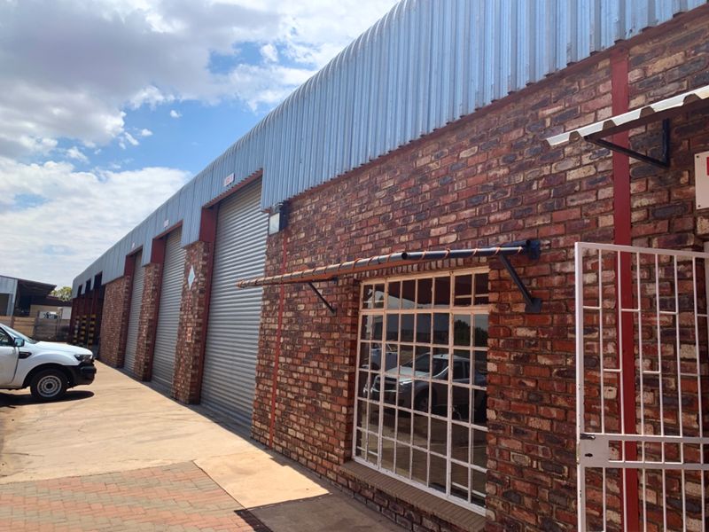 Industrial property exterior featuring face brick walls, corrugated metal roofing, and multiple roller shutter doors with secure steel window frames.