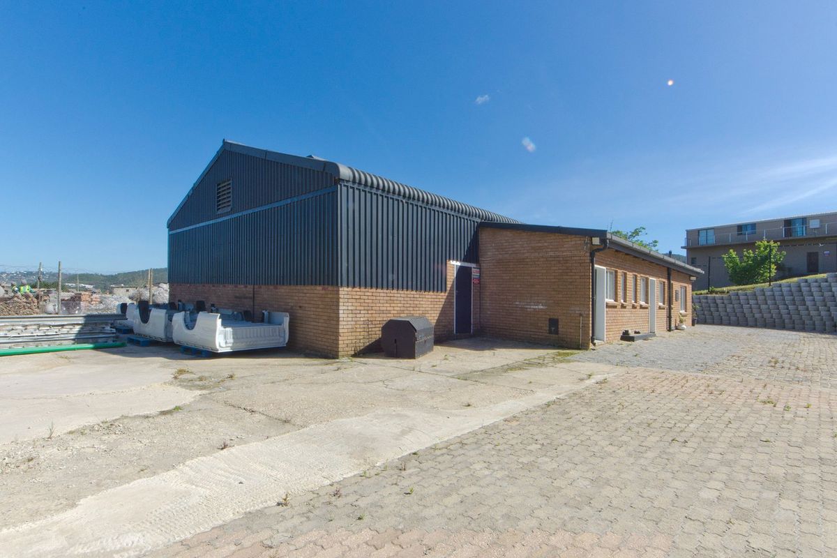 Rear view of an industrial building featuring a combination of face brick and corrugated metal cladding with an adjacent paved yard area.