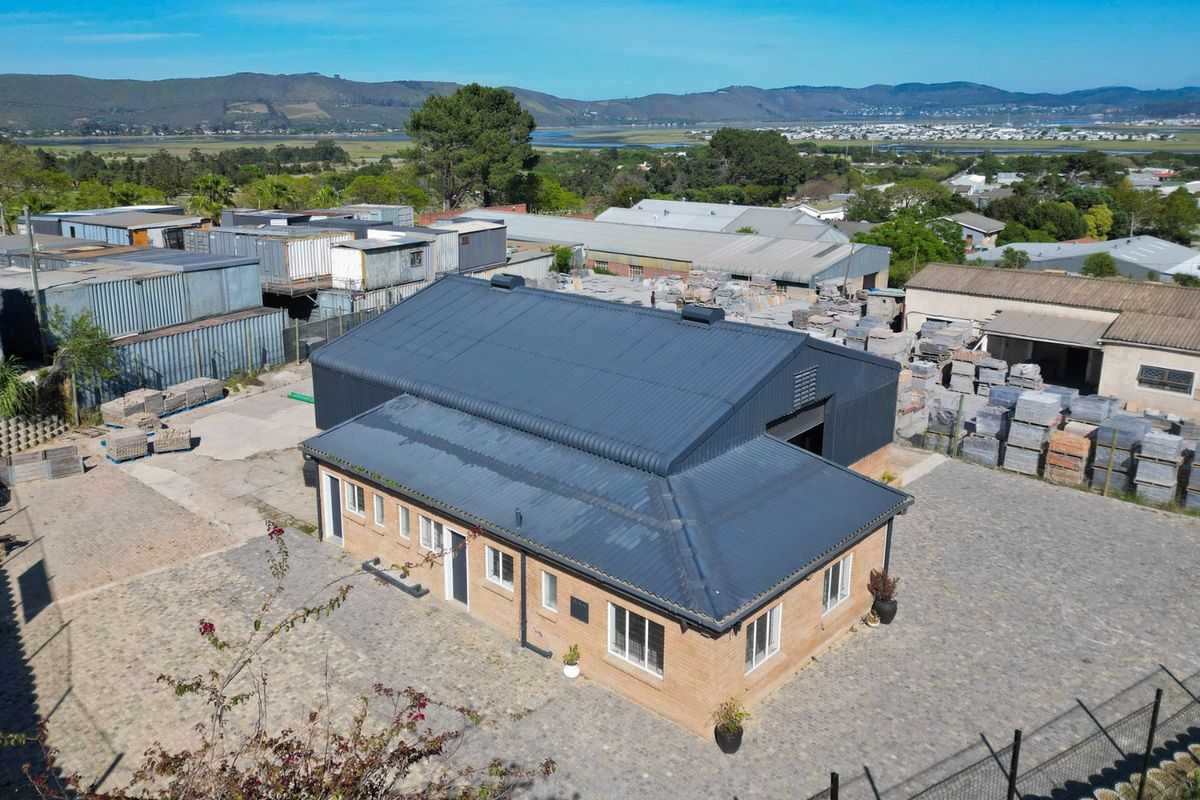 Aerial view of an industrial property featuring a brick building with a corrugated metal roof, situated within a paved yard and surrounding industrial area.
