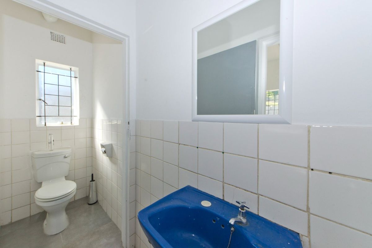 A functional bathroom featuring white wall tiles, a blue basin, and a separate toilet area with a window for natural light.