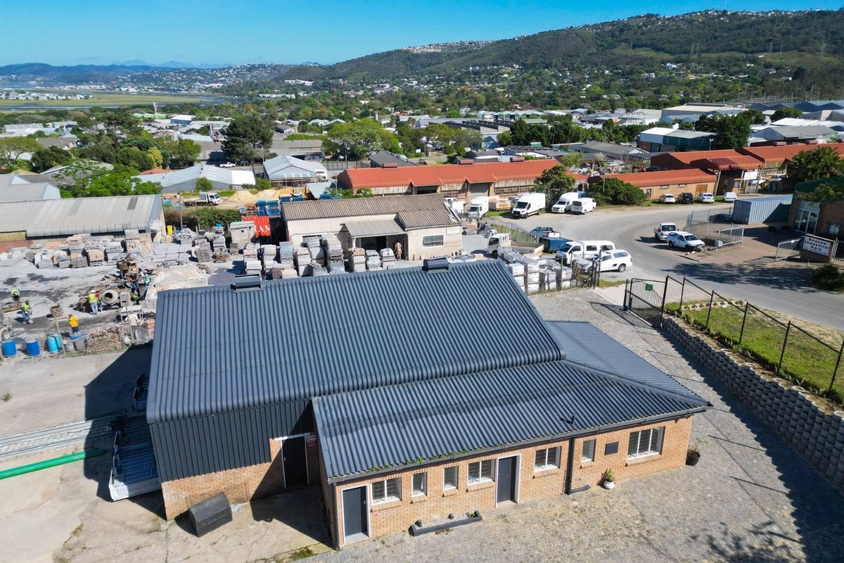 Aerial view of an industrial property featuring a brick building with a corrugated metal roof, paved exterior area, and surrounding industrial park infrastructure.