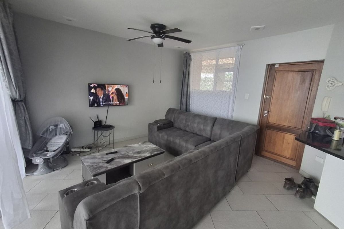 A living room area featuring tiled flooring, a ceiling fan, and a wooden entrance door, providing a functional and open living space.