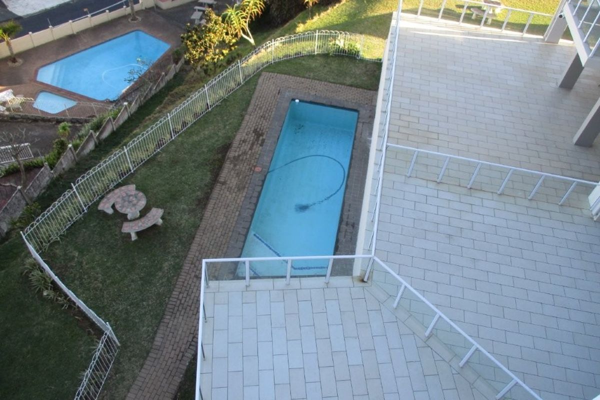 Elevated view of a communal outdoor area featuring a swimming pool, paved patio space, and landscaped garden surroundings.