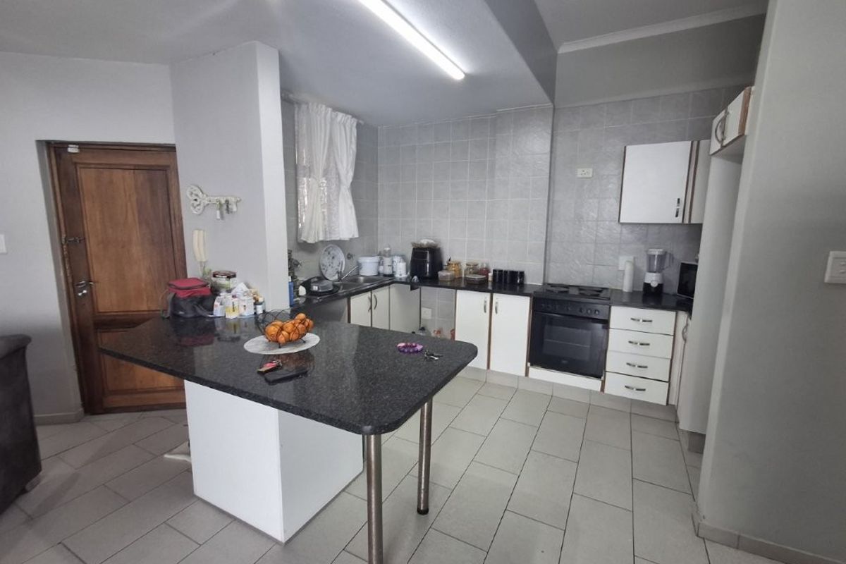 Functional kitchen featuring granite countertops, a central island, built-in oven and hob, and tiled flooring with ample storage cabinetry.