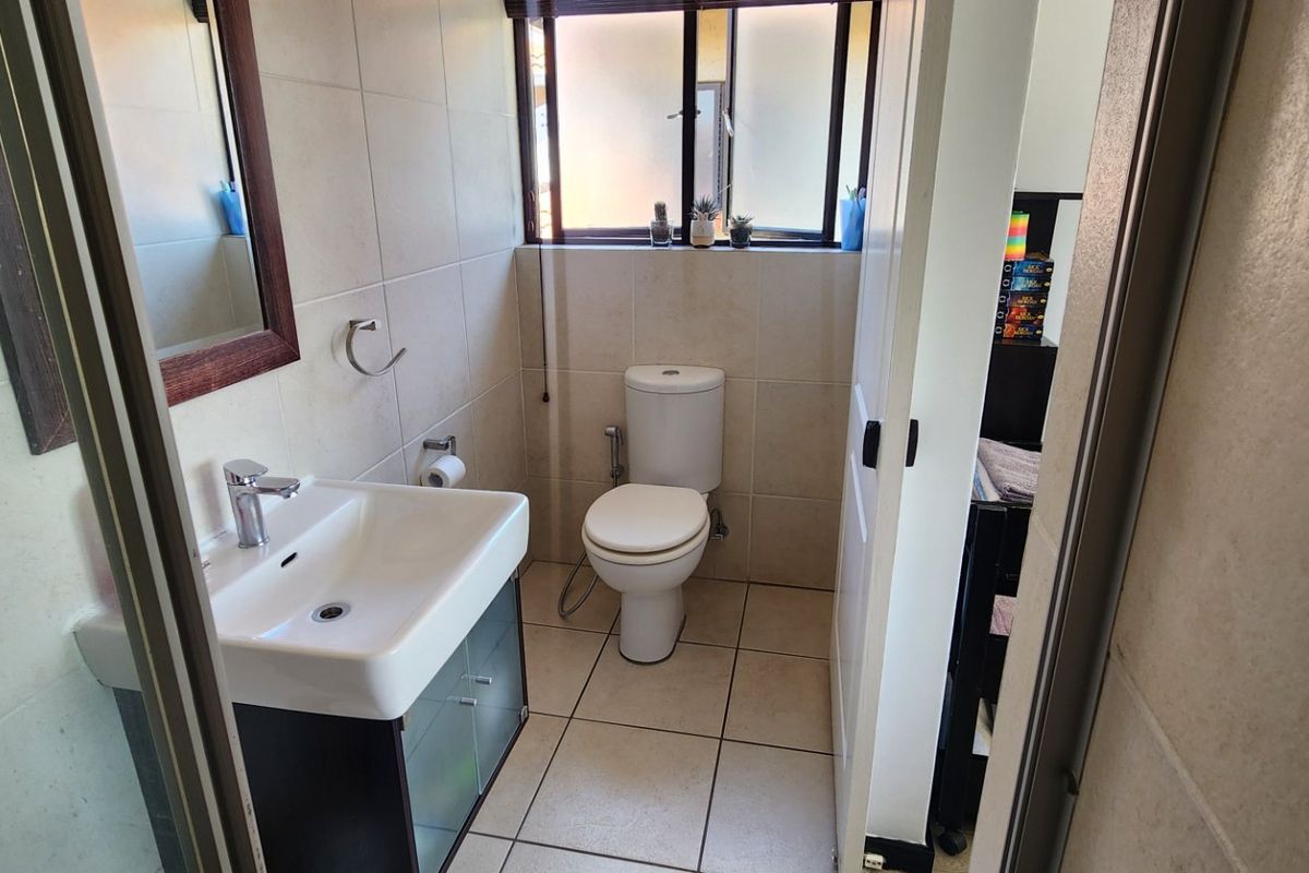 A functional bathroom featuring a vanity cabinet with a ceramic basin, a toilet, and neutral wall and floor tiling.