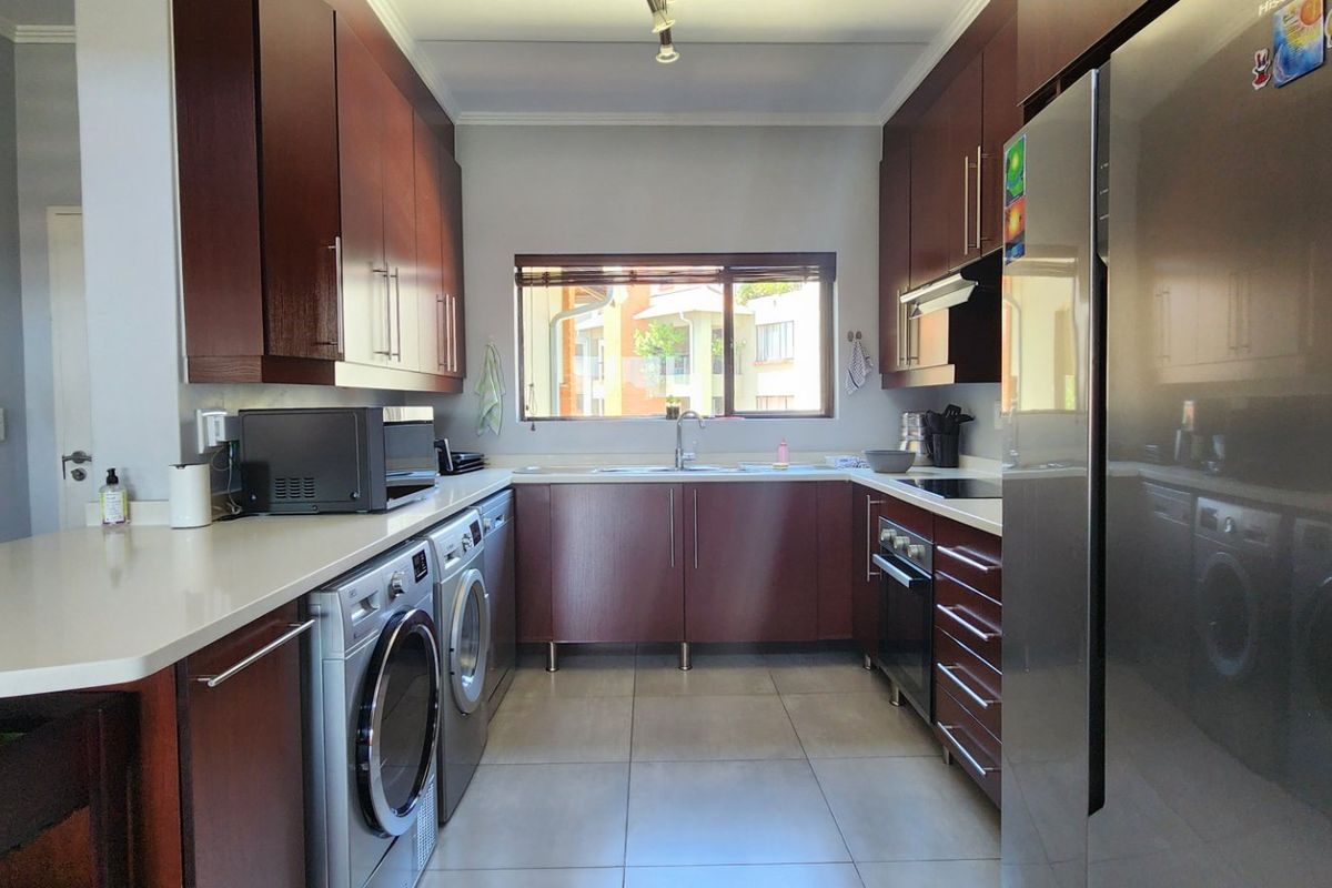 A functional galley-style kitchen featuring dark wood cabinetry, stone countertops, integrated appliances, and tiled flooring with ample storage space.
