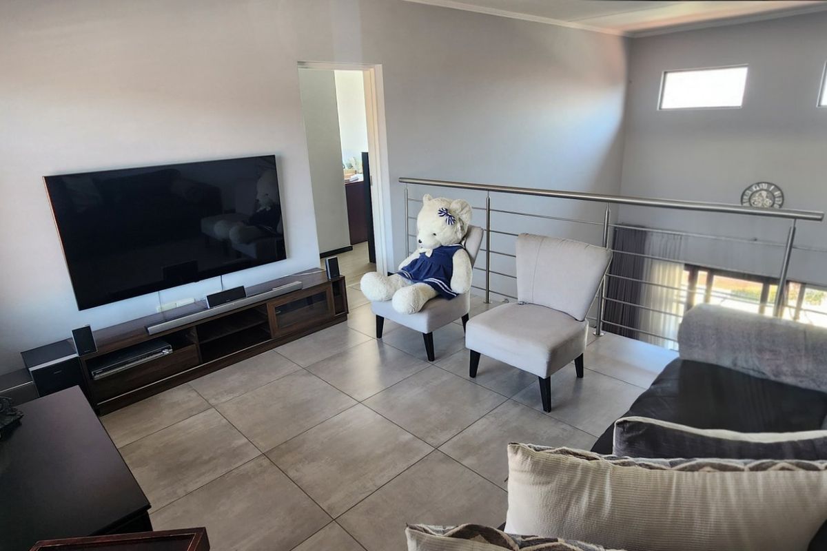 A modern living area featuring large format floor tiles, a stainless steel balustrade overlooking the lower level, and high-set clerestory windows.