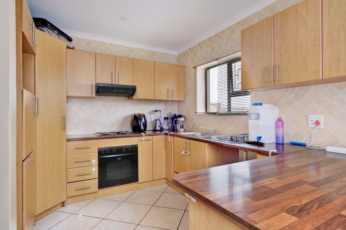 A functional kitchen featuring light wood cabinetry, dark laminate countertops, built-in oven, hob, extractor fan, and tiled finishes throughout.